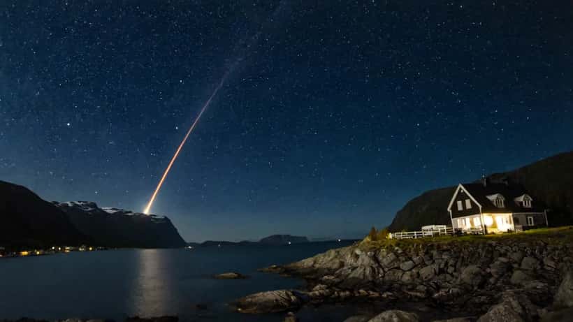 Komet med lysende hale over norsk fjordlandskap om natten