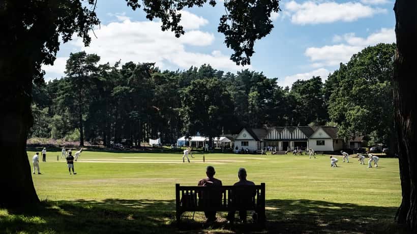 English club cricket match in progress with players and spectators on a summer day