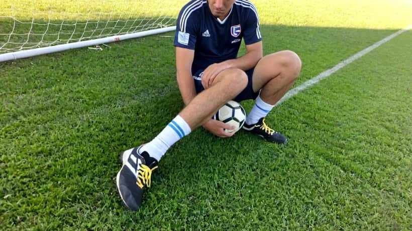 Sportfysiotherapeut onderzoekt enkel van amateurvoetballer op outdoor voetbalveld, illustratie blessurepreventie